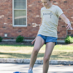 Girl with an Olympia Girl t-shirt kicking a soccer ball