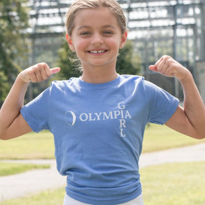 Young girl wearing a blue t-shirt with 'Olympia Girl' text, flexing her muscles outdoors.