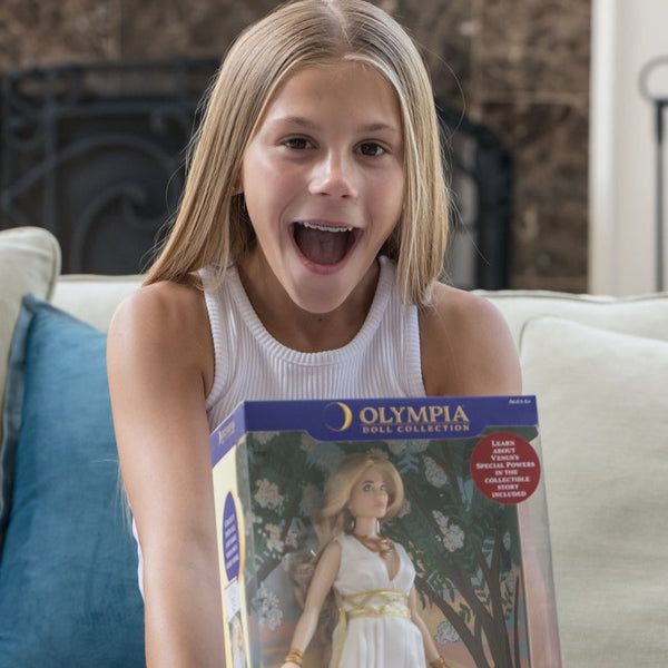 Young girl holding a doll box with a doll named 'Venus' on a couch.