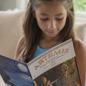 Girl reading a rtemis' Story Card on a couch.