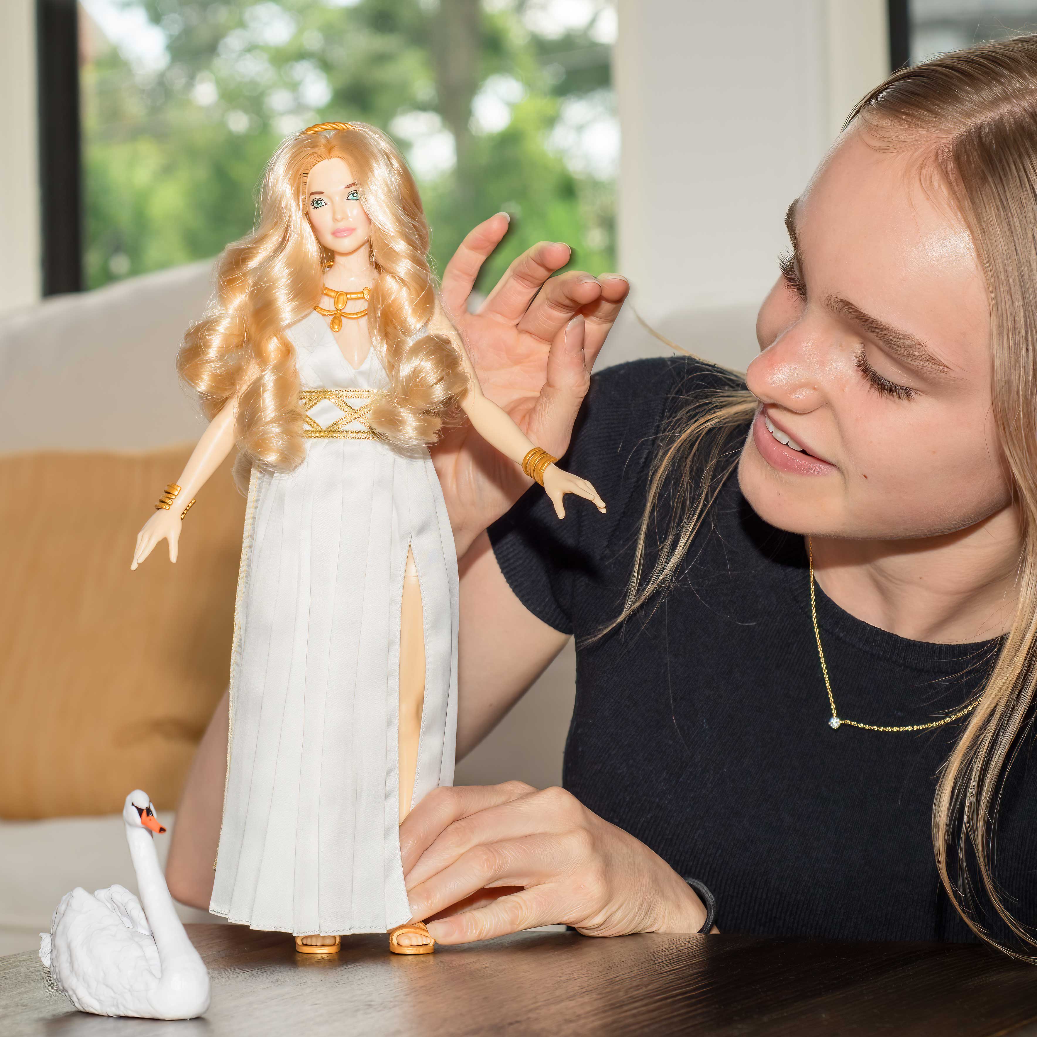 Woman playing with a doll and a swan figurine on a table.