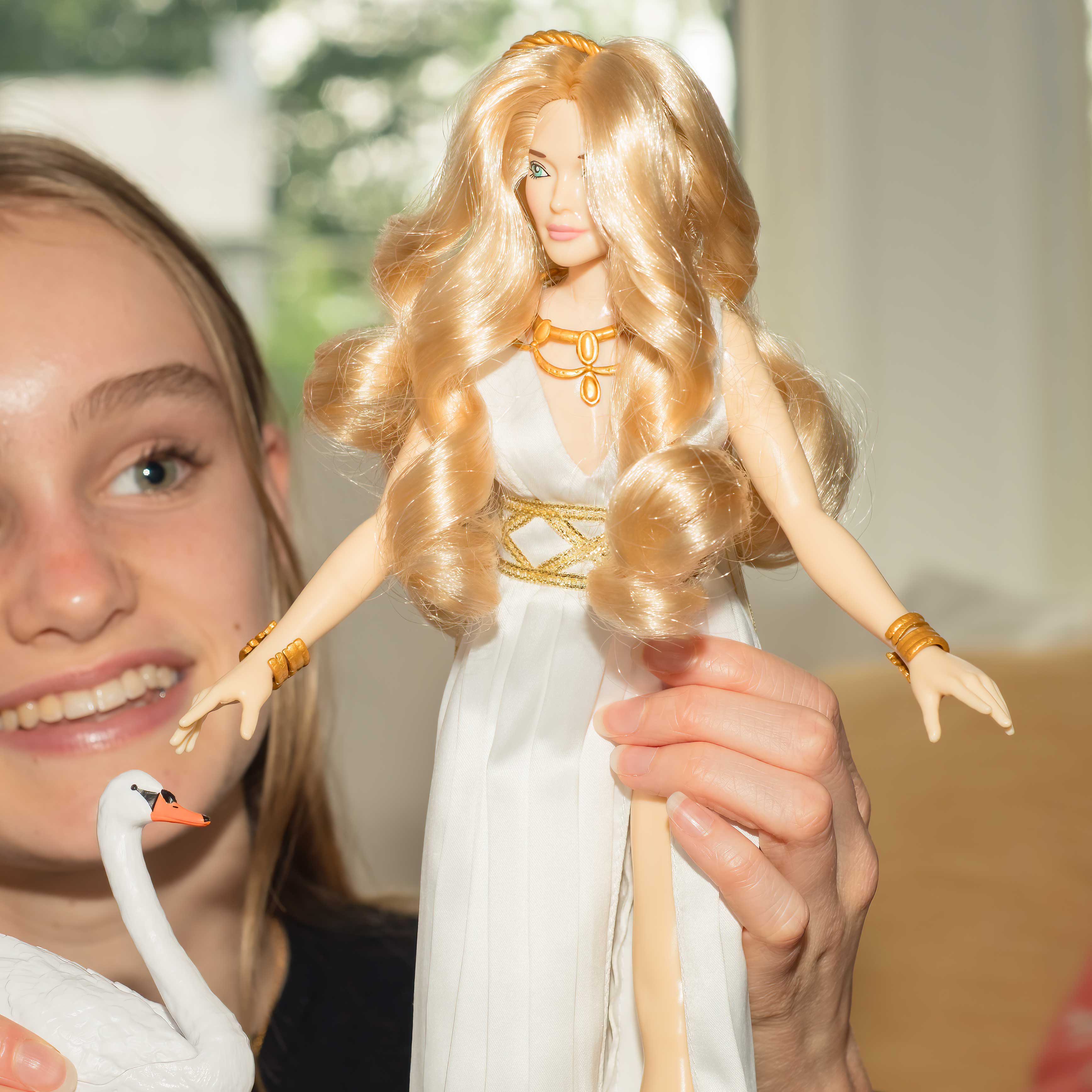 Person holding a doll with long blonde hair and a white dress, with a swan in the foreground.