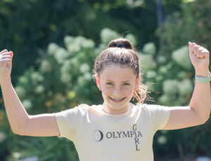 Girl wearing a 'Girl Olympia' t-shirt with arms raised outdoors.