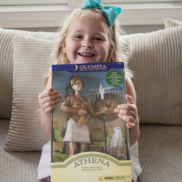 Young girl holding an Athena doll packaging with 'Olympia Doll' branding