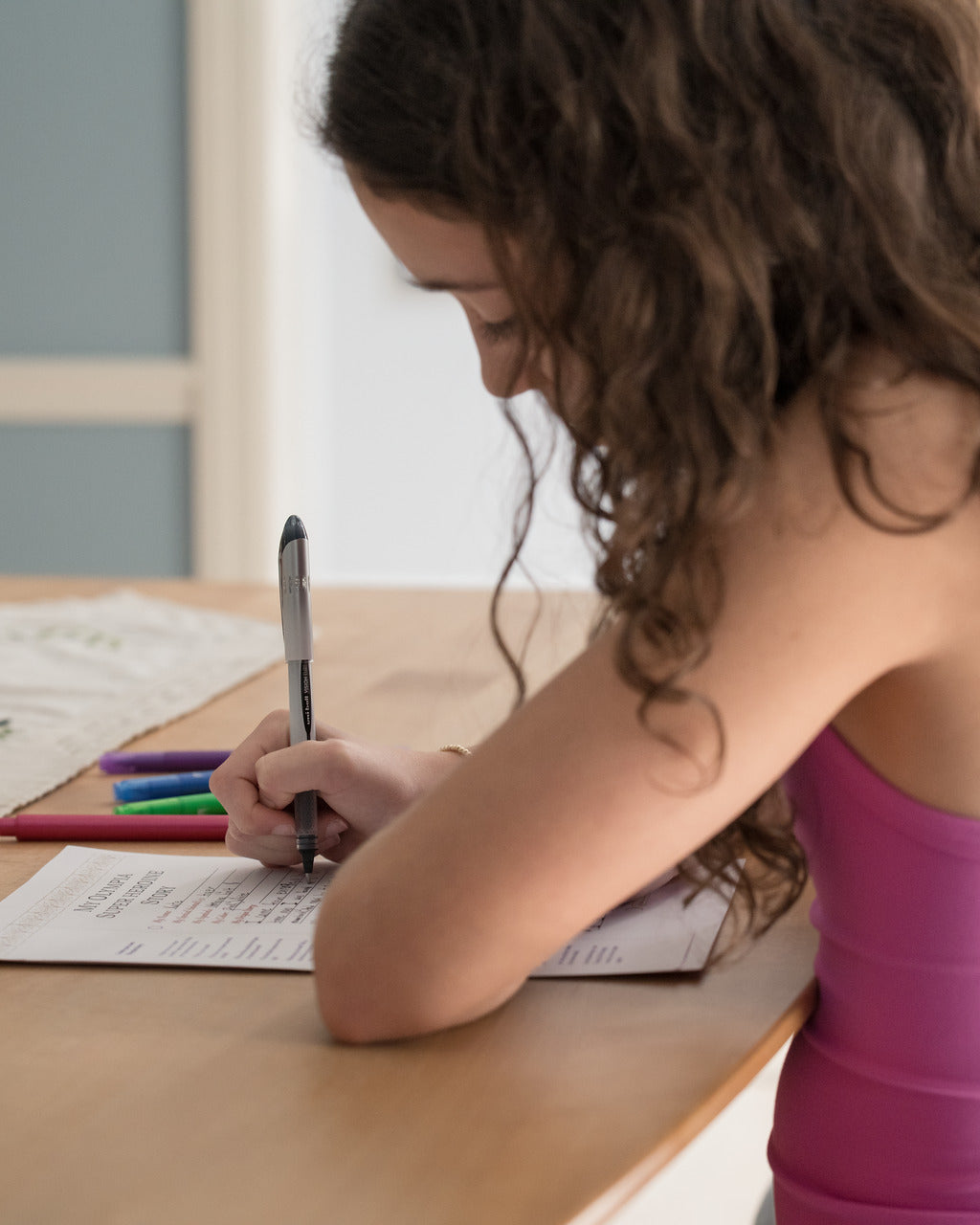 Person writing on a piece of paper with a pen at a desk.