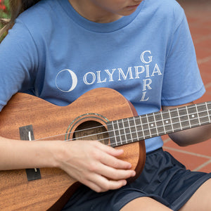 Person playing a ukulele wearing a blue t-shirt with 'Olympia Girl' text.