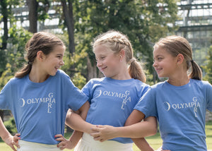 Three girls wearing blue t-shirts with 'Olympia Girl' text, standing outdoors.