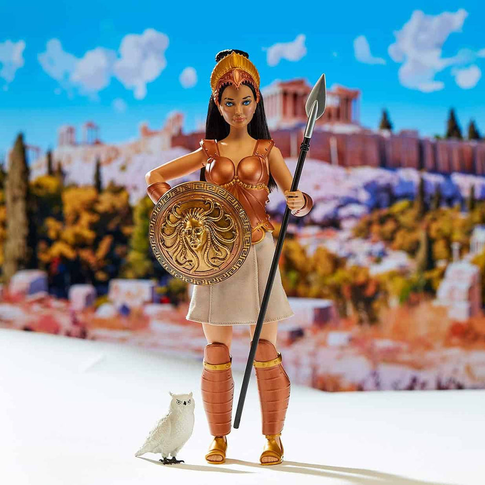 A female warrior action figure stands holding a spear and round shield with a lion emblem, with a small white owl at her feet. The background shows a colorful blurred scene of the Acropolis.